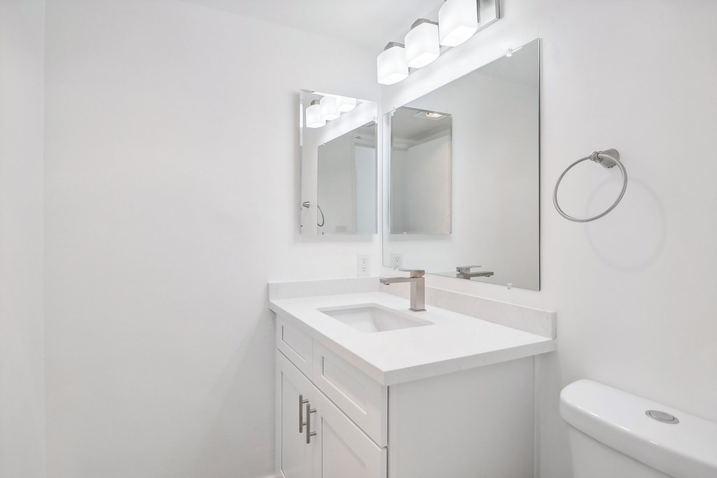 A white bathroom with a sink, mirror, and toilet.
