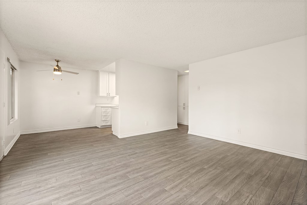 A room with a ceiling fan and light fixture, a small white cabinet, and a wooden floor.