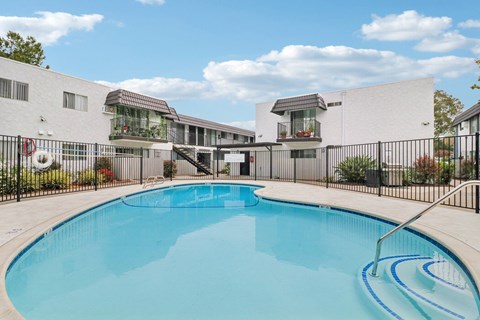 A swimming pool in front of a white building with a black fence around it.