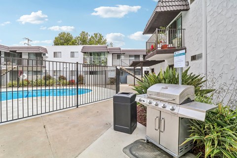 A BBQ grill and trash bin are on a patio next to a pool.