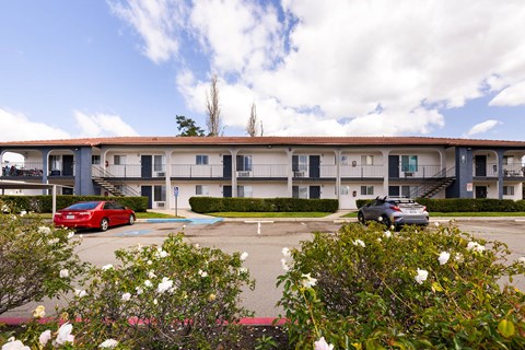 A red car is parked in front of a building with a blue car parked in front of it.