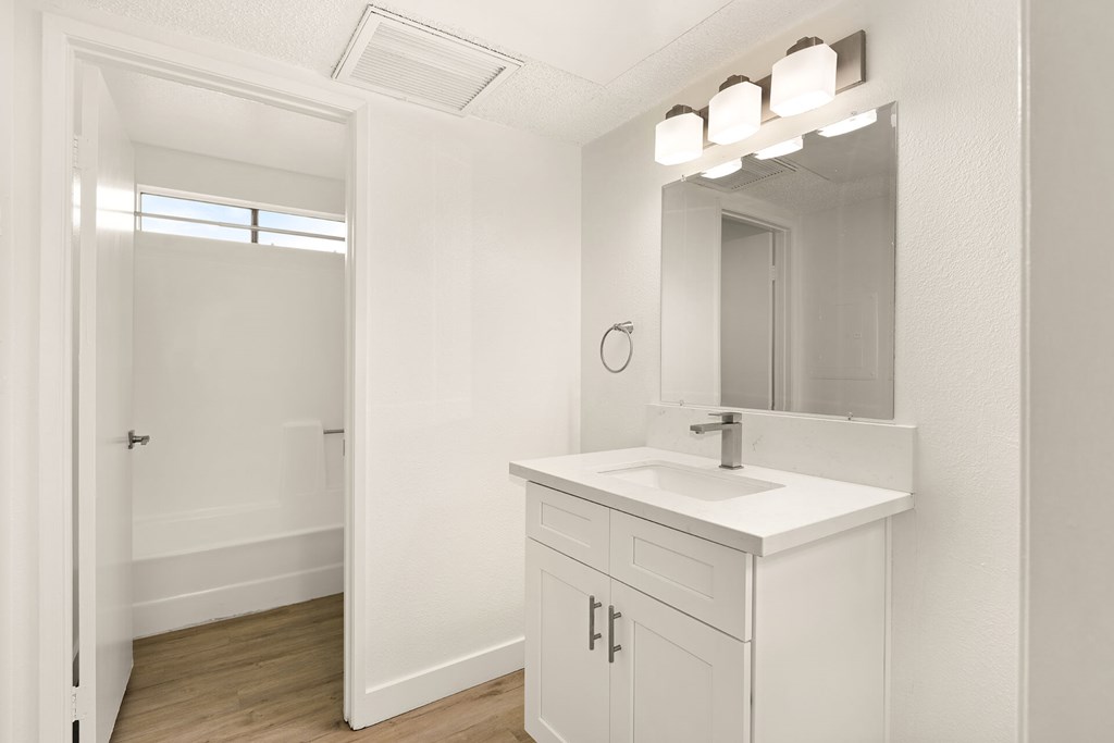 A white bathroom with a sink, mirror, and light fixture.