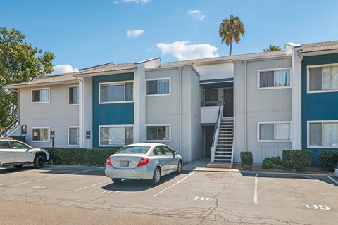 A car is parked in front of a two-story apartment building.