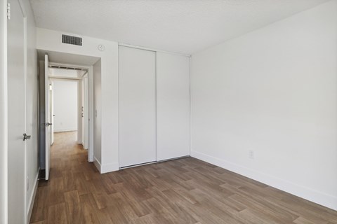 A room with white walls and wood flooring with a doorway leading to another room.