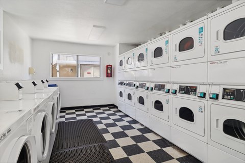 A row of white front load washing machines are lined up in a laundromat.