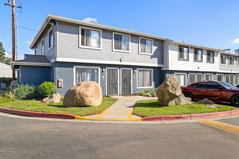 A red car is parked in front of a grey building with a blue door.