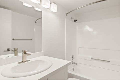 A white bathroom with a sink, mirror, and shower.
