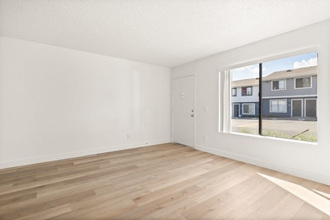 Empty room with wooden flooring and a window showing a building outside.