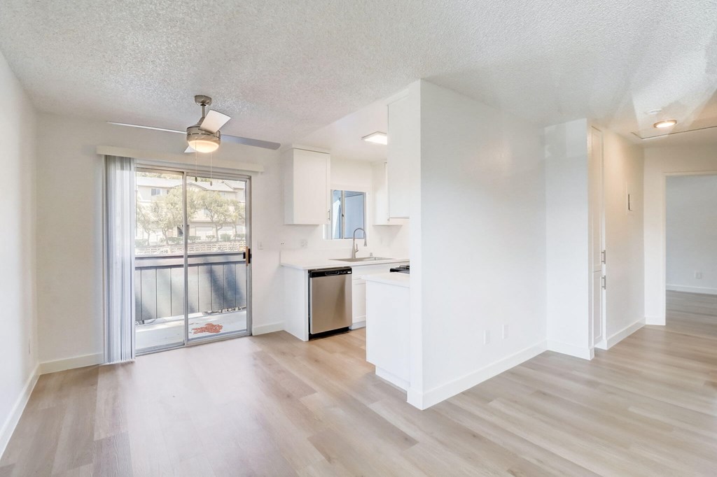 A spacious, empty room with a kitchenette and sliding glass doors leading to a balcony.