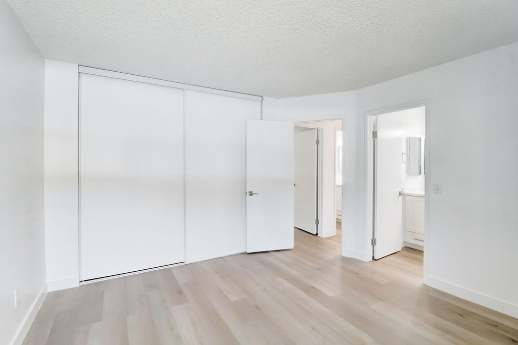 A room with white walls and wooden flooring with three white doors.