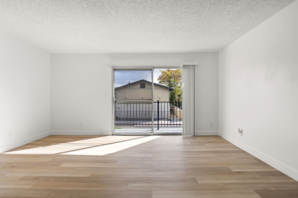 A room with white walls and wooden flooring, leading to a balcony with a railing.