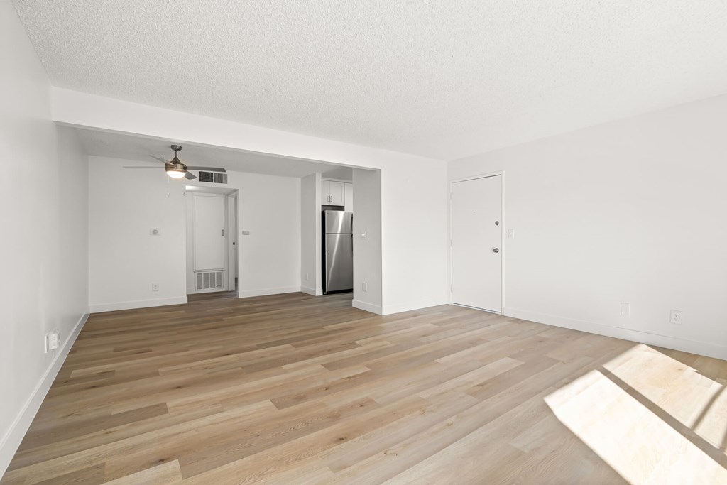 A room with wooden flooring and a refrigerator in the corner.