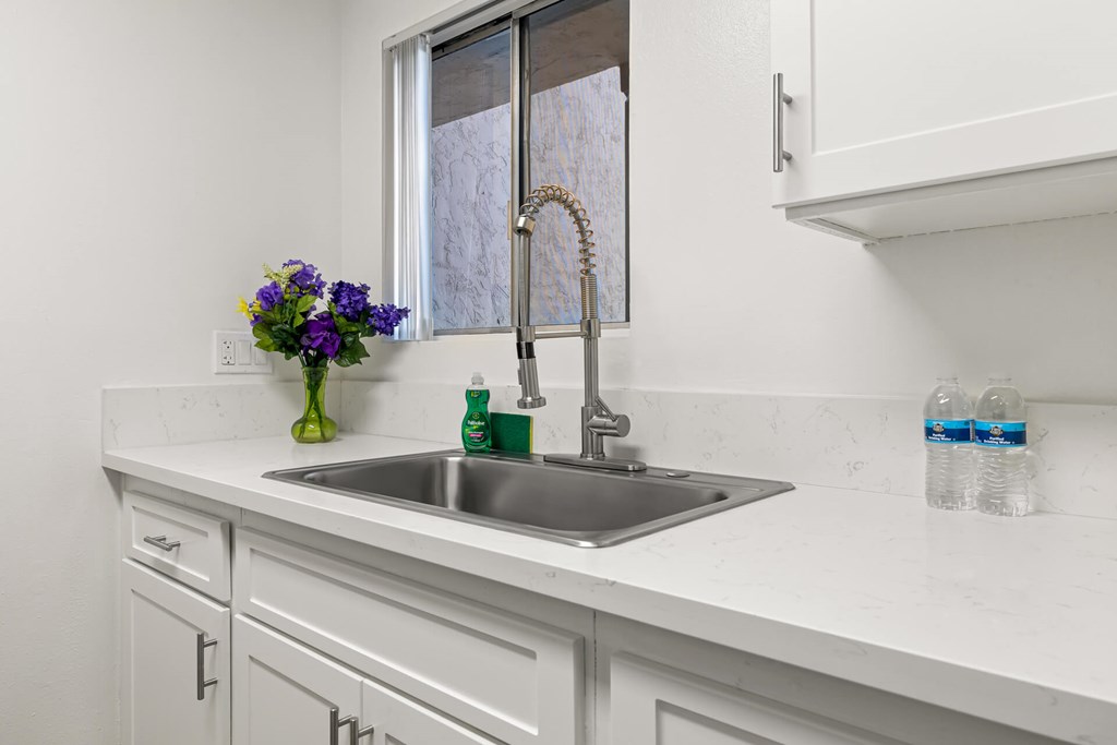 A white kitchen with a silver sink and a window.