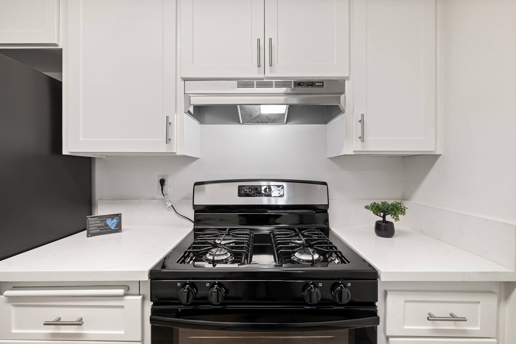 A black stove top oven with four burners and a silver range hood above it.