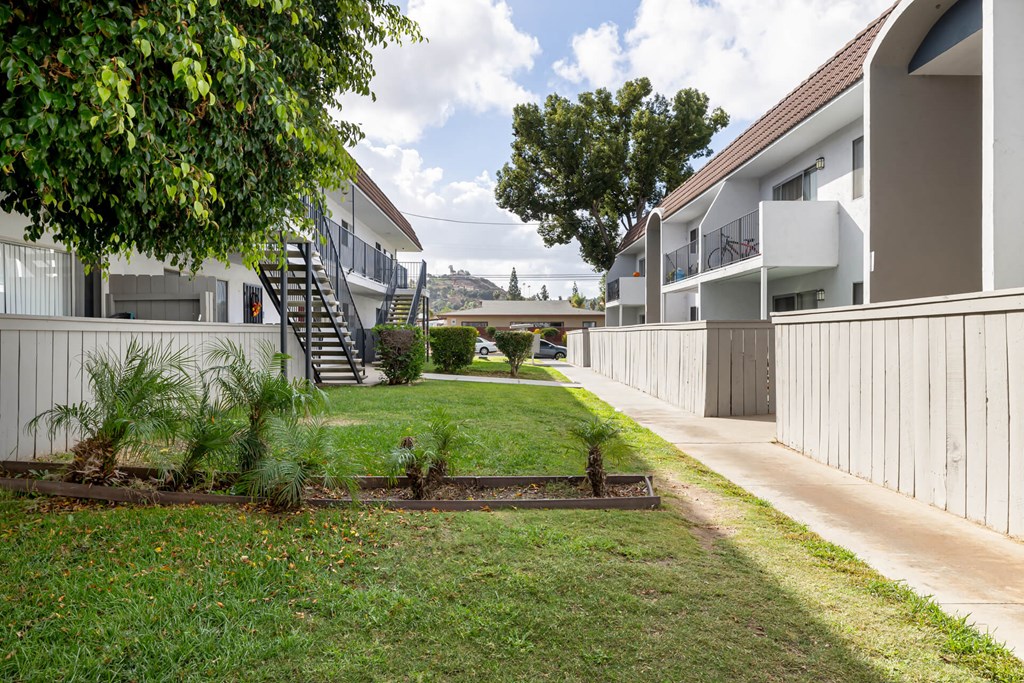 A grassy area in front of a building with a tree and a small garden.