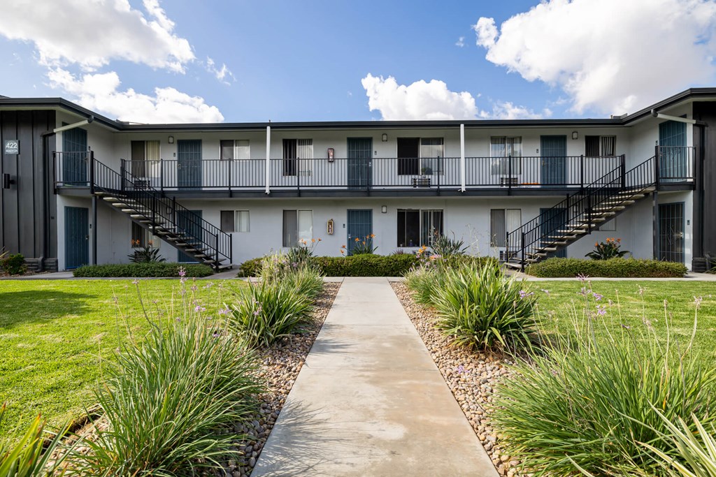 A concrete walkway leads to a white building with black railings and staircases.