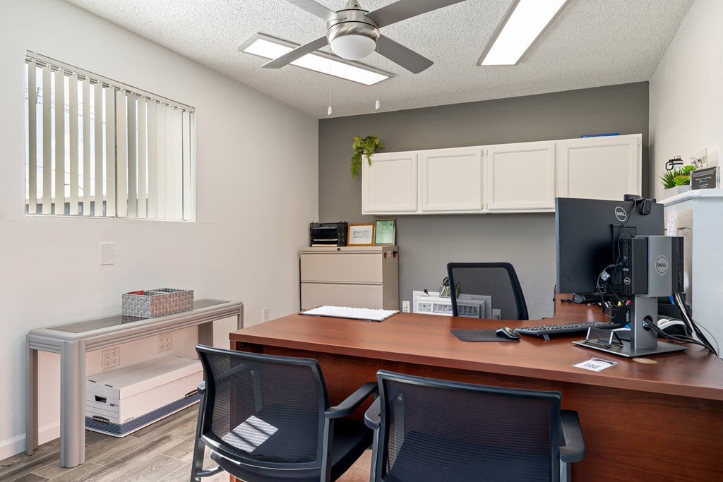 A room with a desk, chairs, and a ceiling fan.