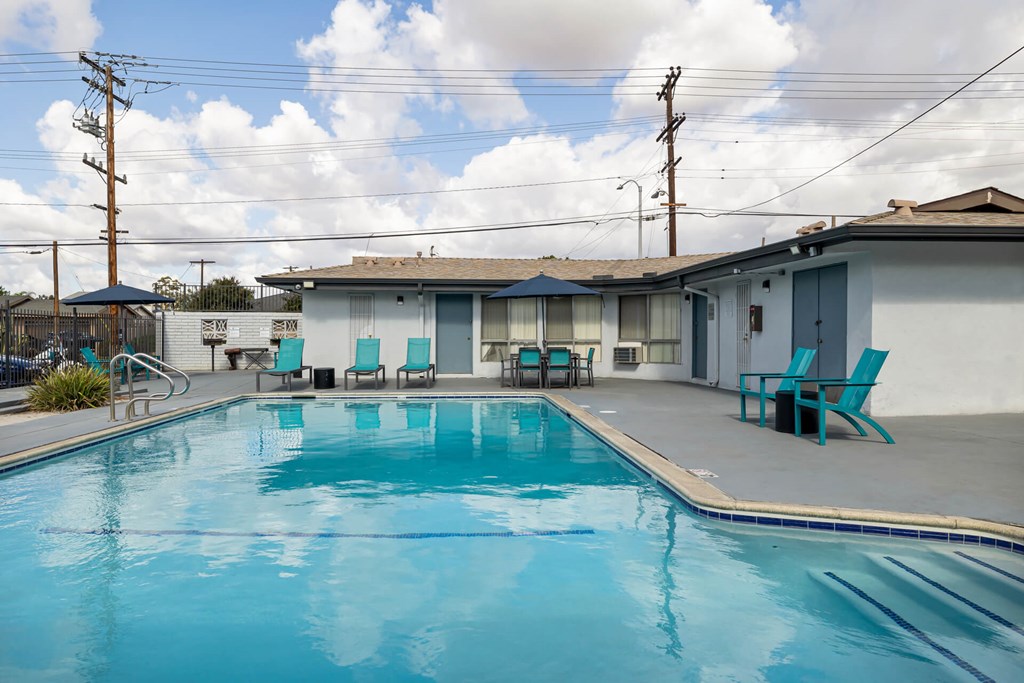 A swimming pool in front of a house with blue chairs around it.
