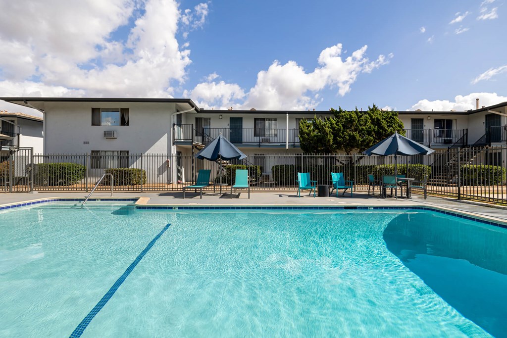 A swimming pool in front of a white building with blue umbrellas and chairs.