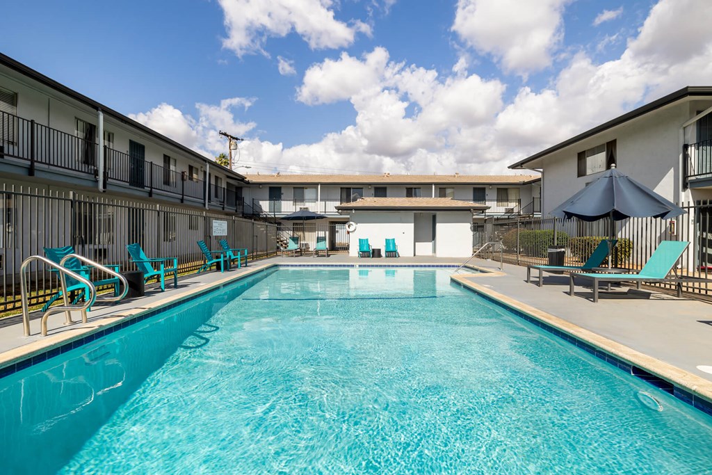A large swimming pool in front of a building with lounge chairs and umbrellas.