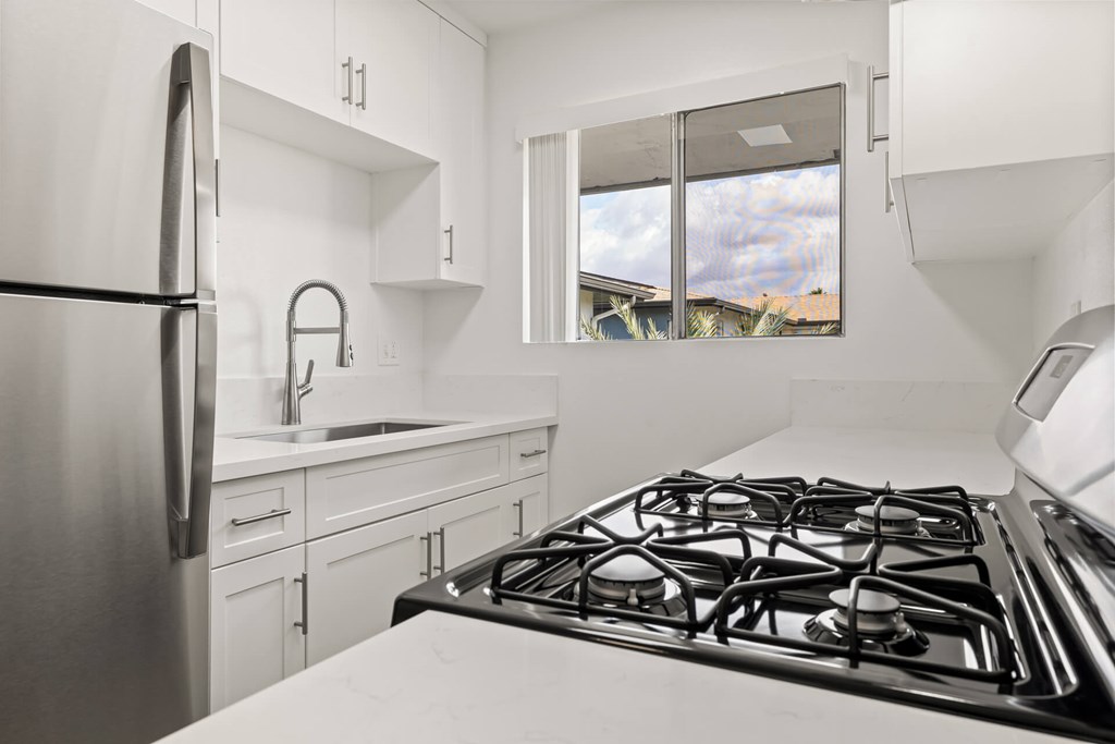A modern kitchen with a stainless steel refrigerator, a stove, and white cabinets.