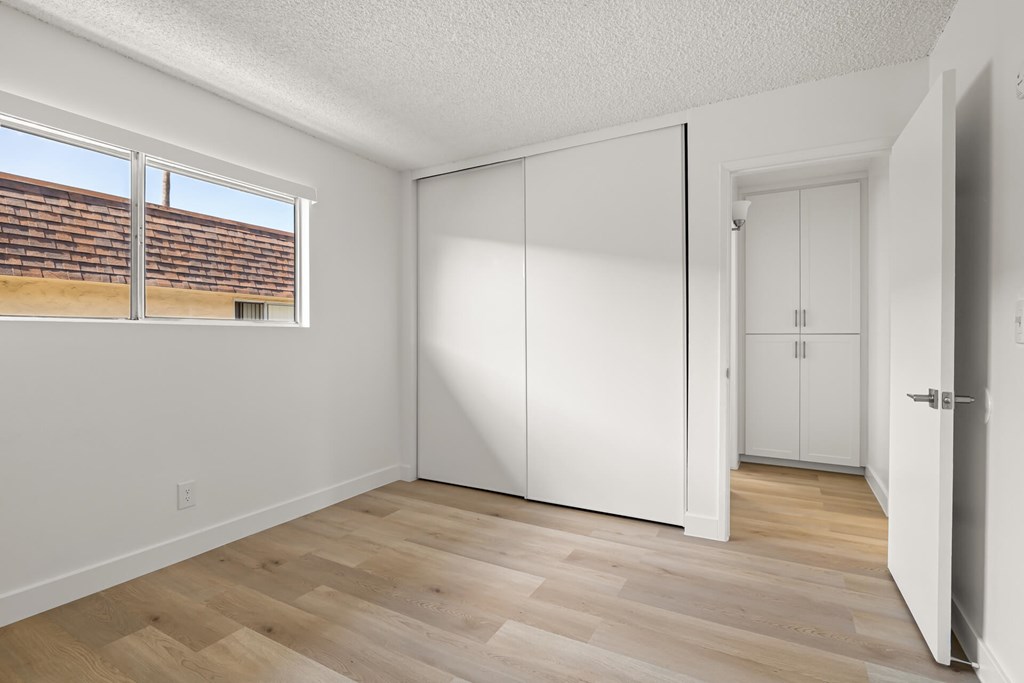 A room with white walls and wooden flooring with a window.