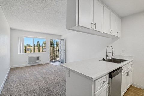 A kitchen with white cabinets and a white countertop with a sink and dishwasher.