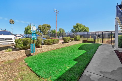 A green sign is on a post in front of a grassy area.