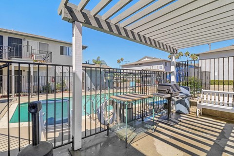 A pool area with a table and chairs under a pergola.