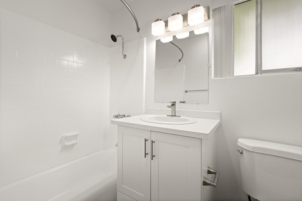 A white bathroom with a sink, mirror, and tub.
