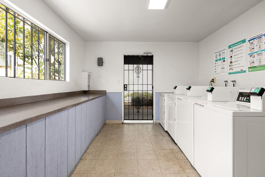 A clean, white-walled laundry room with a row of washers and dryers.