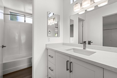 A white bathroom with a sink, mirror, and a window.