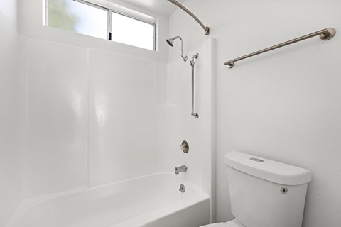 A white bathroom with a tub, toilet and grab bars.