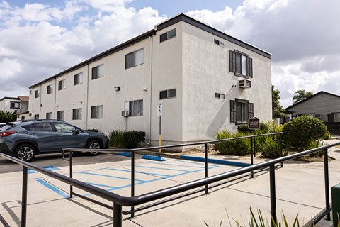 A parking lot in front of a white building with a blue car parked in the spot.