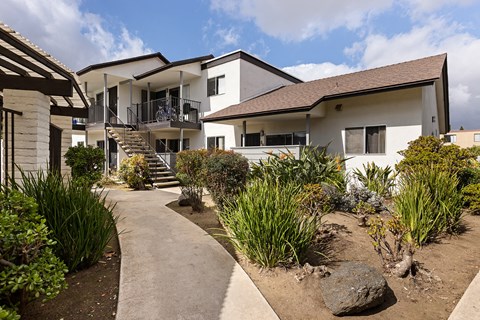 A white building with a brown roof and a concrete walkway in front of it.