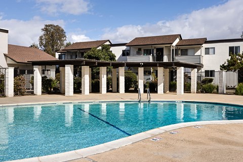 A swimming pool in front of a house with a white fence.