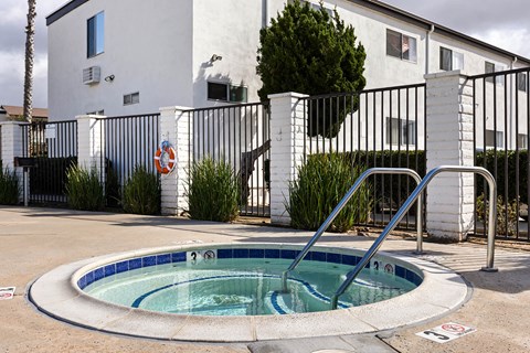 A small pool in front of a white building with a black fence.