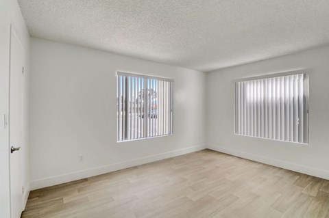 A room with wooden flooring and two windows with blinds.