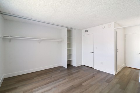 A room with white walls and wooden flooring with a closet and a door.