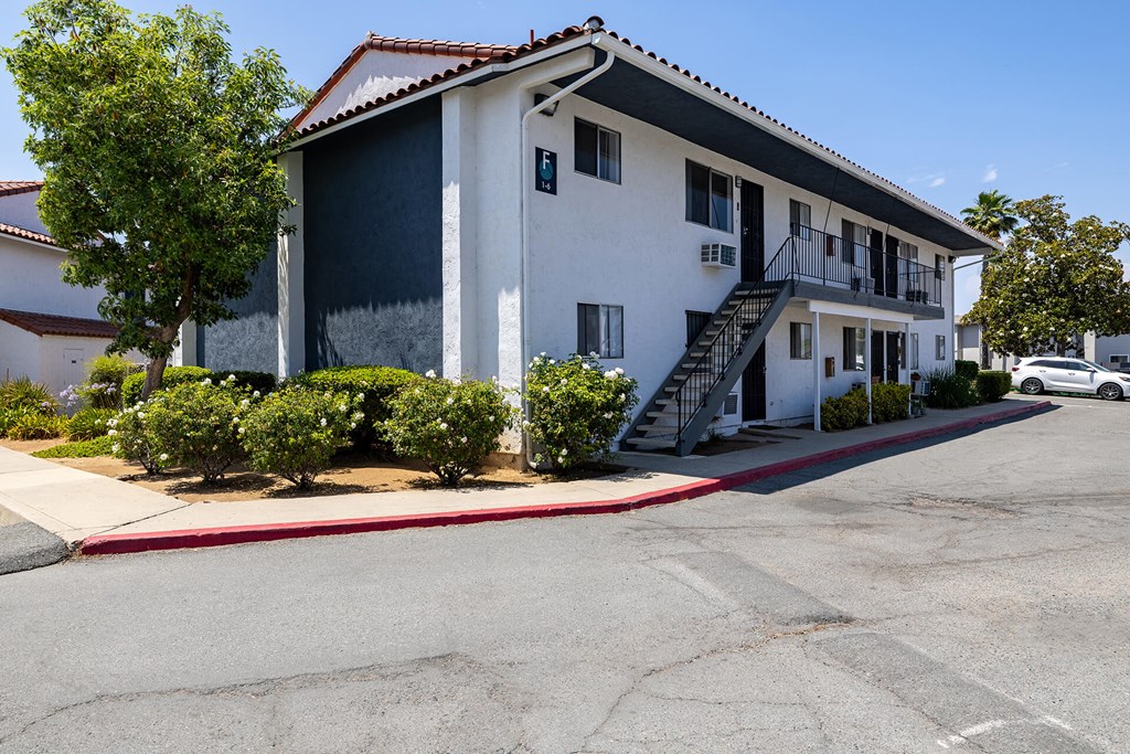 A white building with a red tile roof and a parking lot in front.