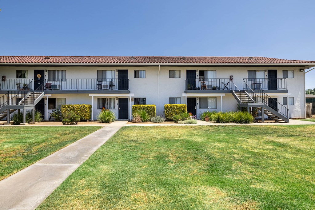 A white building with a red tile roof and a green lawn in front.