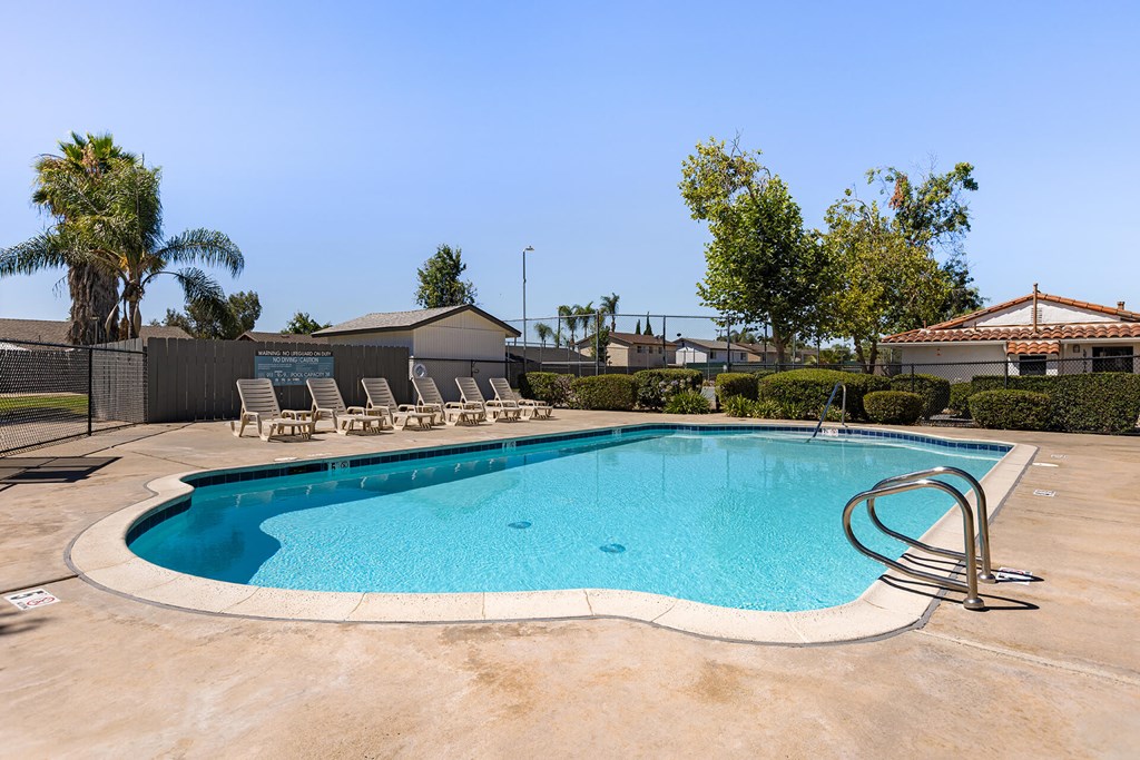 A swimming pool with a diving board and lounge chairs.