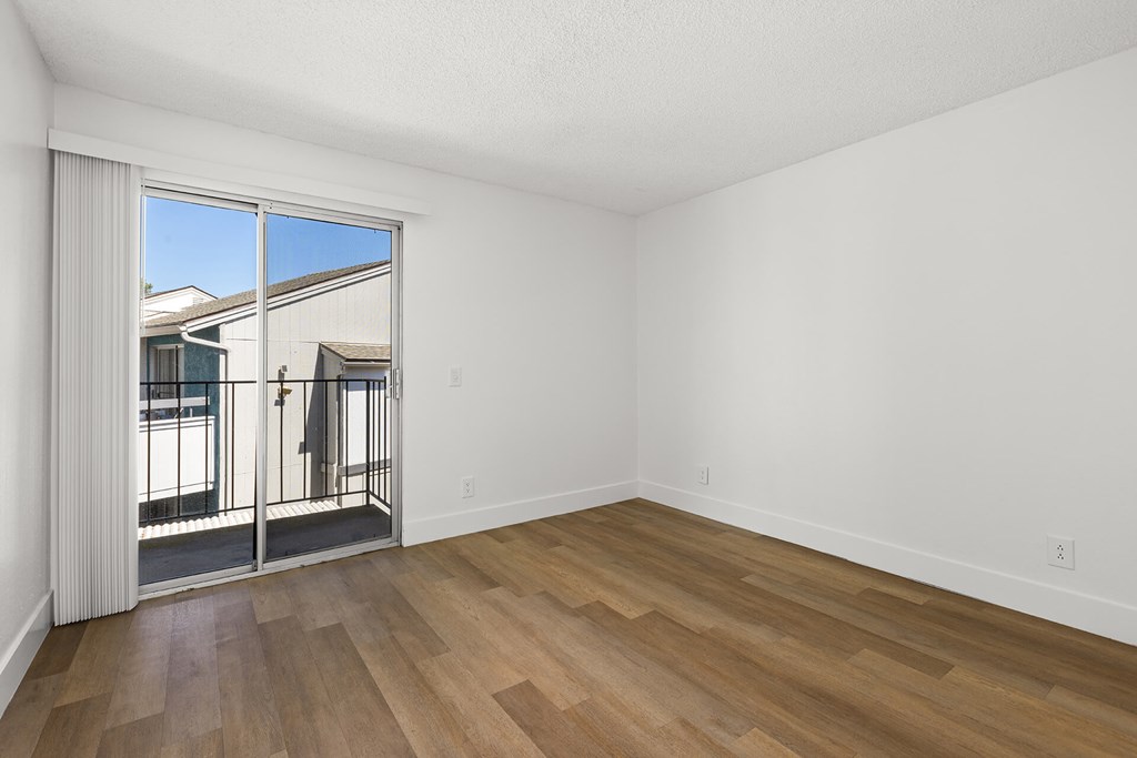 A room with wooden flooring and a large window overlooking a balcony.