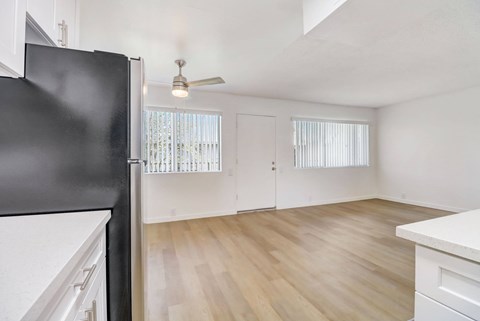 A black fridge in a kitchen with white cabinets and a wooden floor.