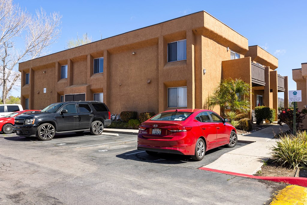 A red car is parked in front of a tan building.