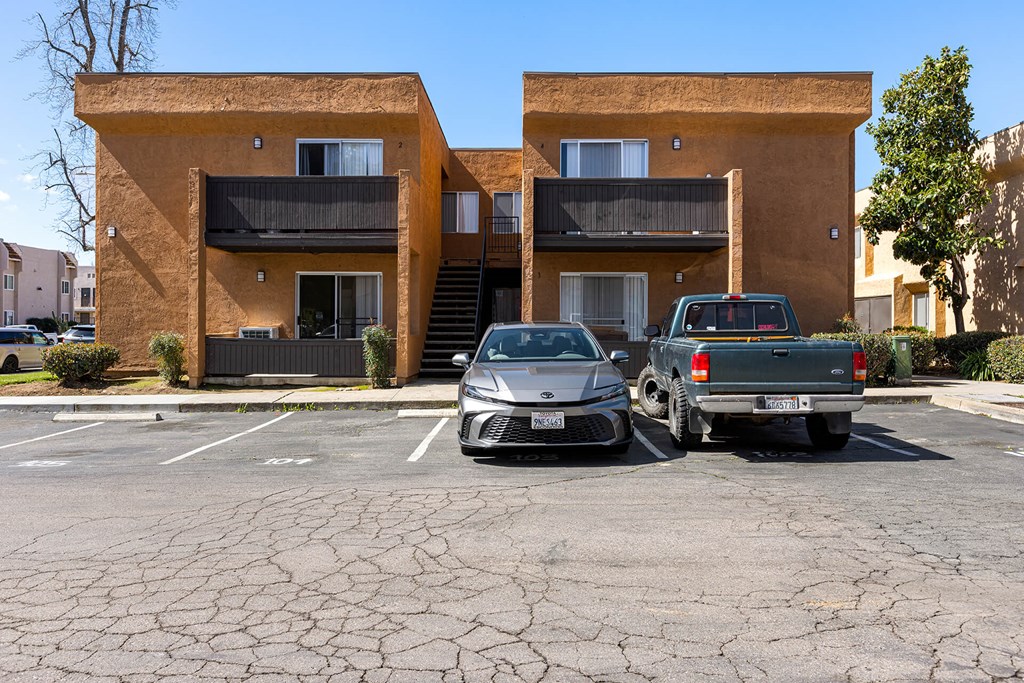 Two cars are parked in a cracked parking lot in front of a tan apartment building.