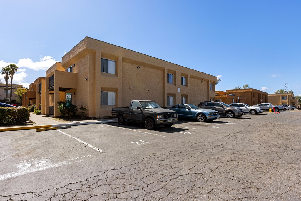 A parking lot in front of a tan building with cars parked.