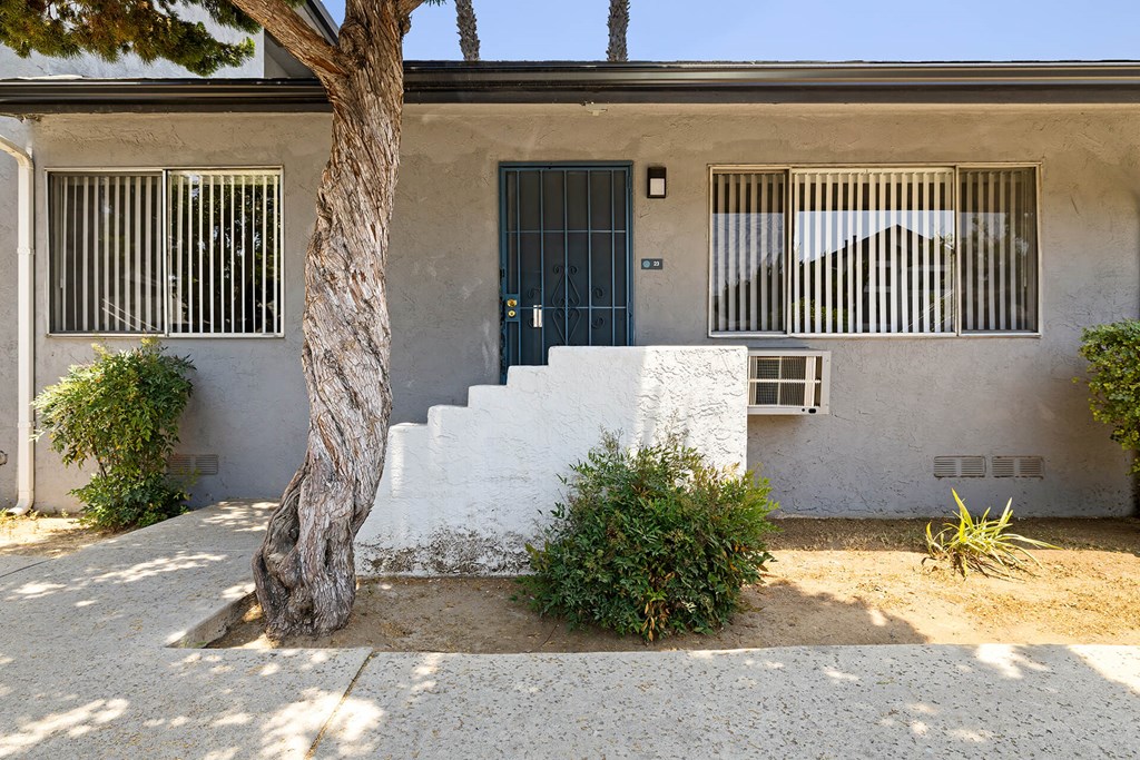 A white house with a blue door and a tree in front.
