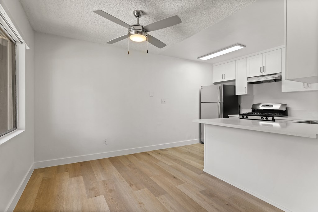 A kitchen with a white ceiling fan and wooden floors.