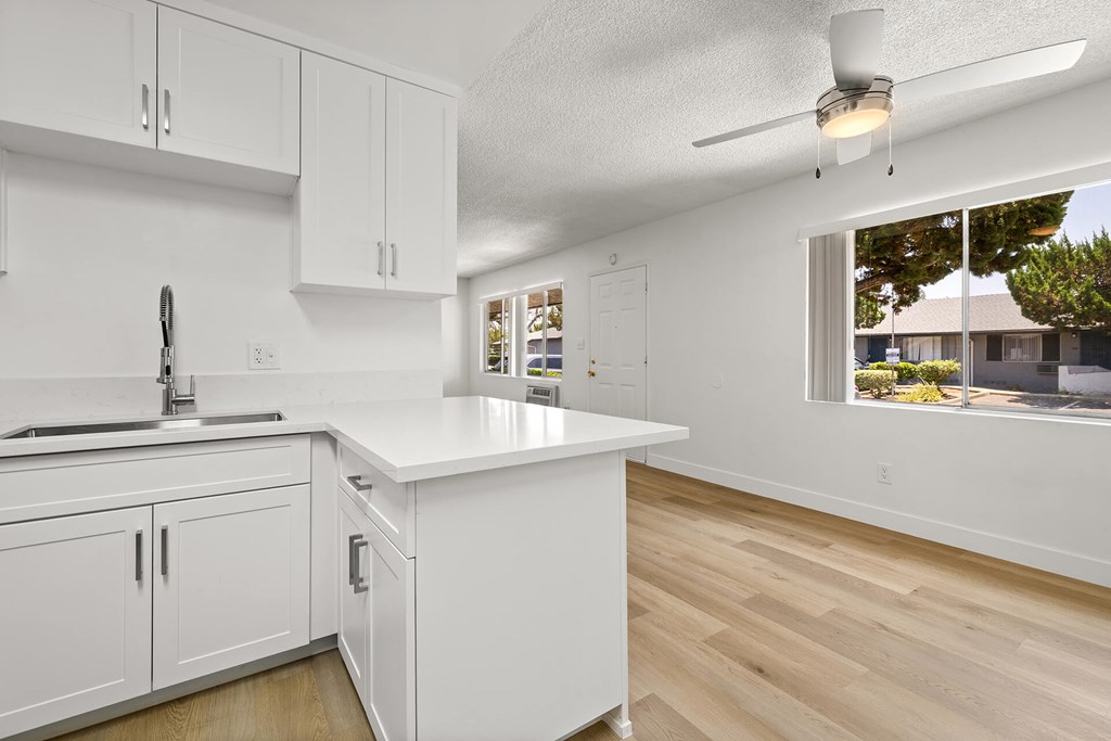 A kitchen with white cabinets and a window overlooking a backyard.